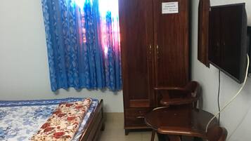 Un dormitorio con cama, un armario de madera, un escritorio con silla y un televisor montado en la pared.