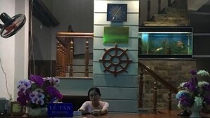A reception area with a clock, a ship's wheel decoration, and a reception desk. - Thanh Trinh Guest House (Binh Kien)