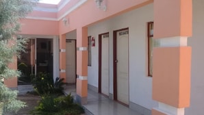 A building with a pink facade, multiple doors, and a small garden area with plants. - Kutse Guesthouse (Letlhakeng)