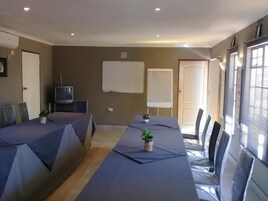 Un salón de conferencias con una larga mesa, sillas, una pizarra y una televisión.