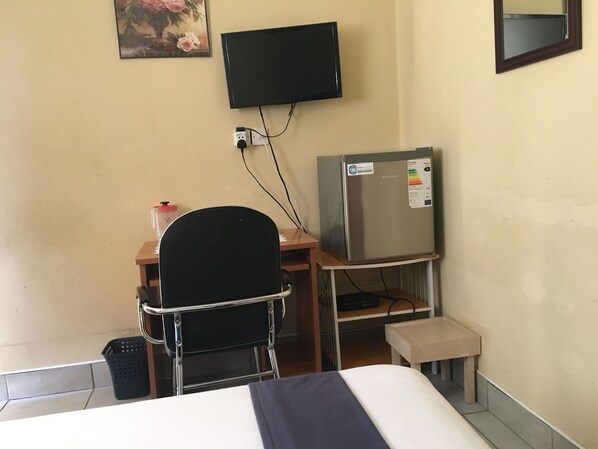 Habitación de hotel con cama, escritorio con silla, refrigerador, televisor montado en la pared y una mesita.