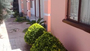 A building with pink walls and white trim, featuring a covered walkway and several doors. - Kutse Guesthouse (Letlhakeng)