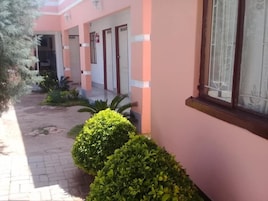 Un edificio con paredes rosadas y detalles blancos, que presenta un corredor cubierto y varias puertas.