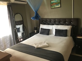 Habitación de hotel con una cama grande, una mesita de noche, una lámpara, un espejo y una ventana con cortinas.