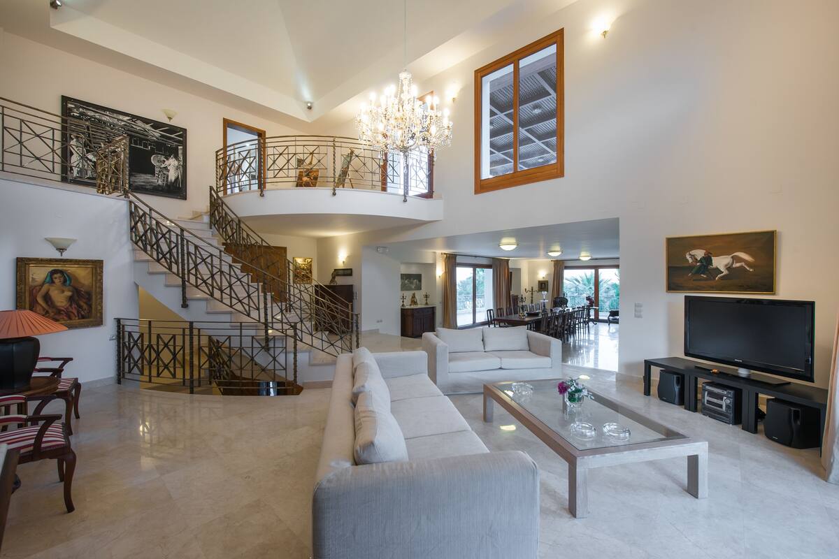 A spacious living area with a large sofa, a coffee table, and a TV. There is a staircase leading to an upper level with a balcony.