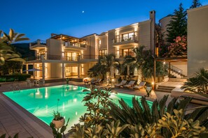 A multi-story building with a swimming pool, outdoor seating, and a staircase leading to the upper floors. - Mansion by Estia (Malevizi)