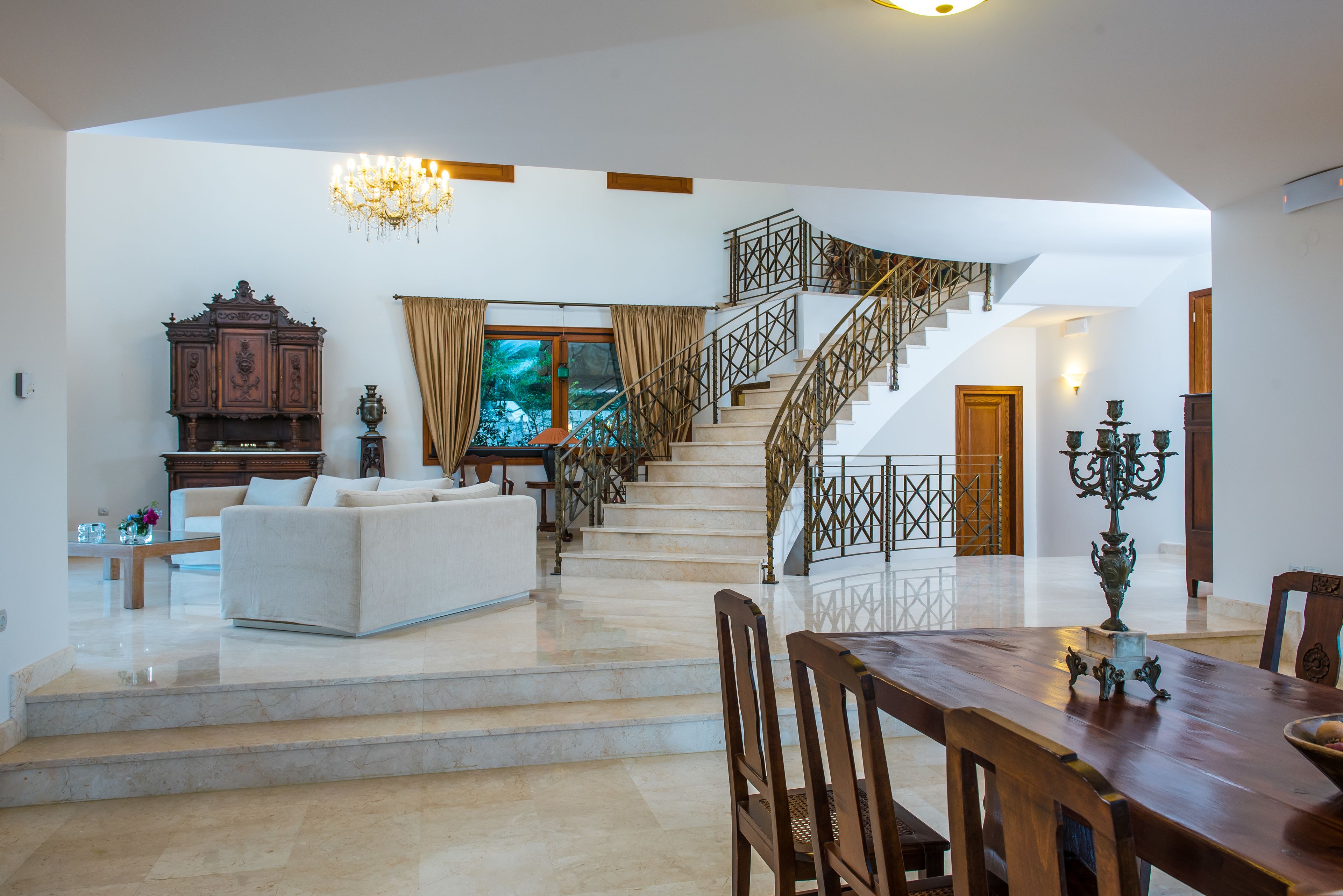 A spacious living area with a staircase, a chandelier, and a dining table.