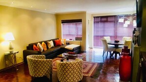 Una sala de estar con sofá, sillones estampados, una mesa de centro y un comedor con mesa y sillas.