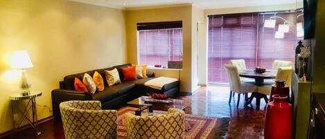 A living room with a sofa, patterned armchairs, a coffee table, and a dining area with a table and chairs.