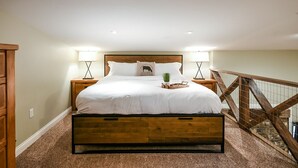 A bedroom with a wooden bed, two bedside tables, a nightstand, a lamp, a decorative pillow, and a small plant.