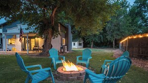 A backyard with a fire pit, four Adirondack chairs, and a house with a porch.