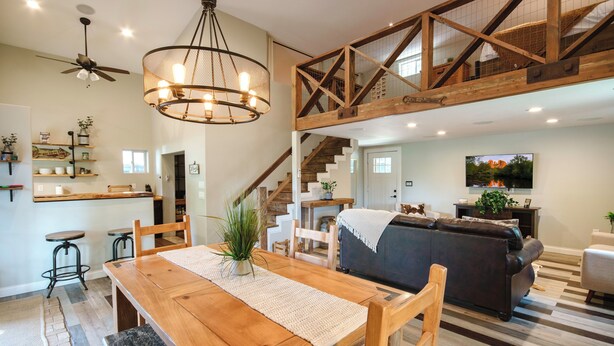 A spacious living area with a wooden dining table, a sofa, and a staircase leading to an upper level.