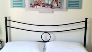 A bed with white bedding and a black metal frame, a wall with a decorative sign that reads "Love the Beach," and two blue shutters. - Casa Malò (Ischia)