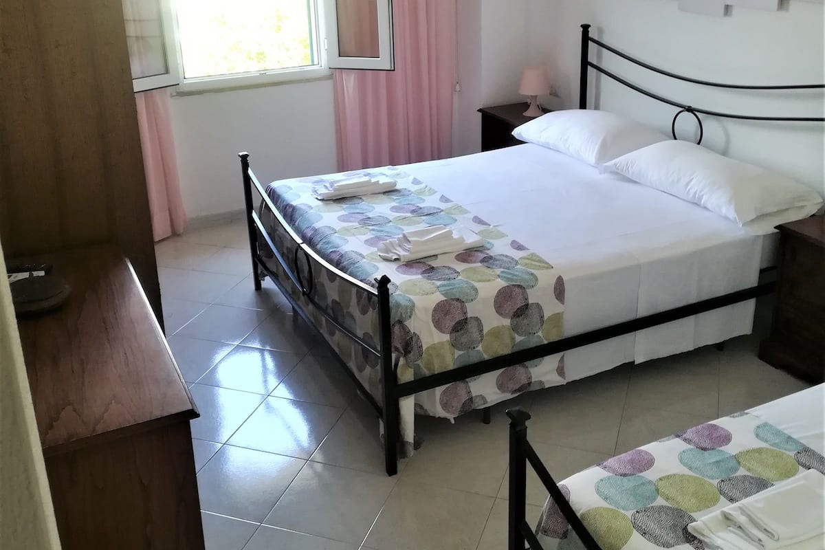 A bedroom with a bed, a desk, a chair, and a window with curtains.
