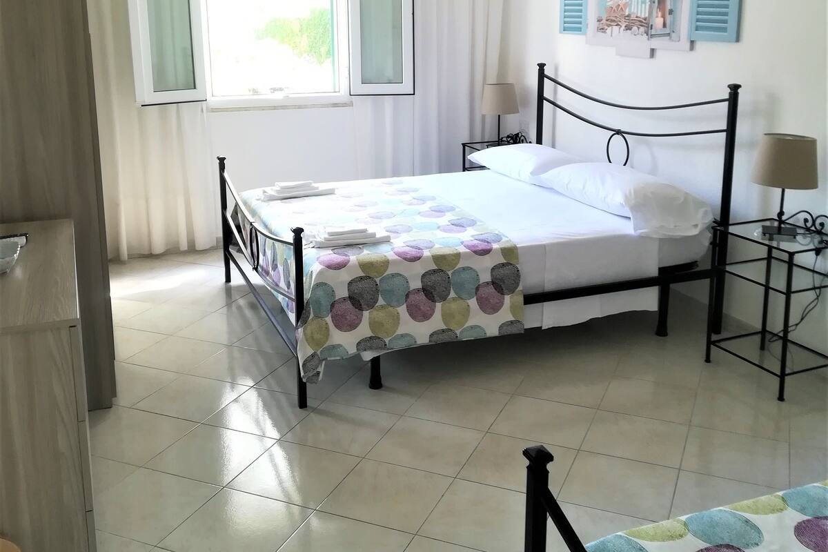 A bedroom with a bed, bedside tables, a window with curtains, a wall decoration, and a hanging light fixture.