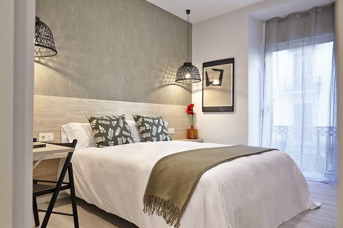 A neatly arranged bedroom with a bed, bedside table, lamp, and a window with curtains.