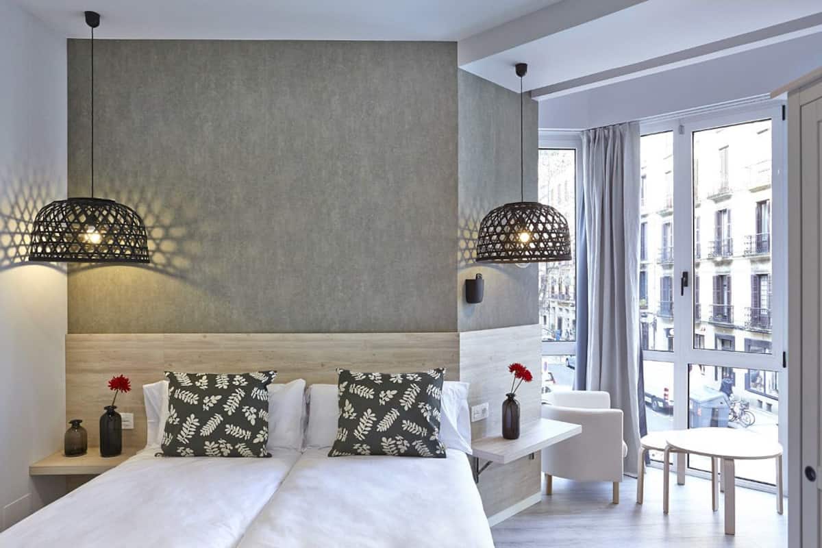 A modern hotel room with a large bed, two pendant lights, a view of the city, and a small table with chairs.