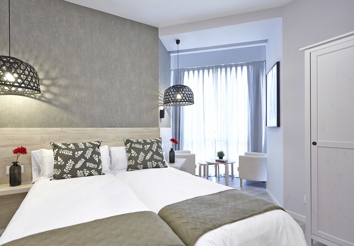 Habitación de hotel moderna con una cama grande, dos lámparas colgantes, una pequeña mesa y vistas al exterior a través de amplios ventanales.
