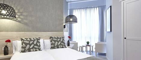 Habitación de hotel moderna con una cama grande, dos lámparas colgantes, una pequeña mesa y vistas al exterior a través de amplios ventanales.
