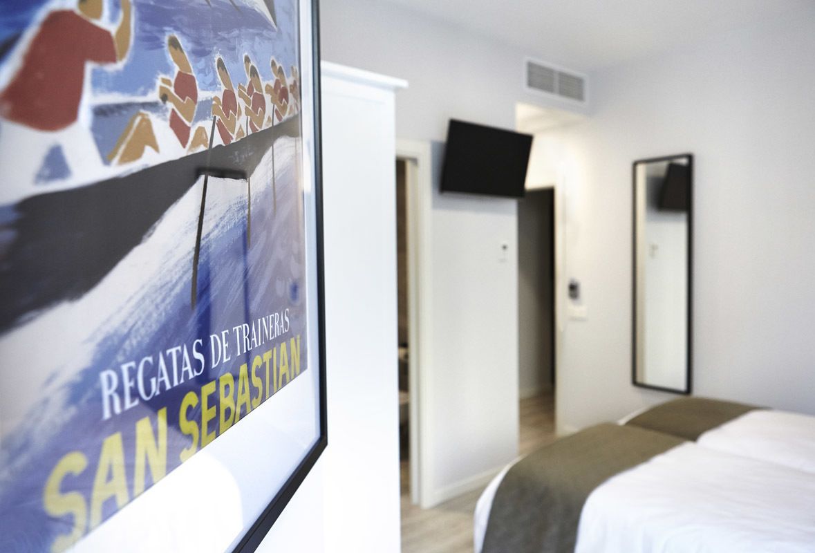 A hotel room with a bed, a TV mounted on the wall, and a poster on the wall.