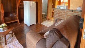 A wooden interior with a sofa, a refrigerator, and a kitchen area. - Cozy chalet in Brotas, SP - Rustic area + Air conditioning (Santa Cecilia II)