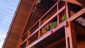 A wooden balcony with multiple levels, potted plants, and a hanging light fixture. - Cozy chalet in Brotas, SP - Rustic area + Air conditioning (Santa Cecilia II)
