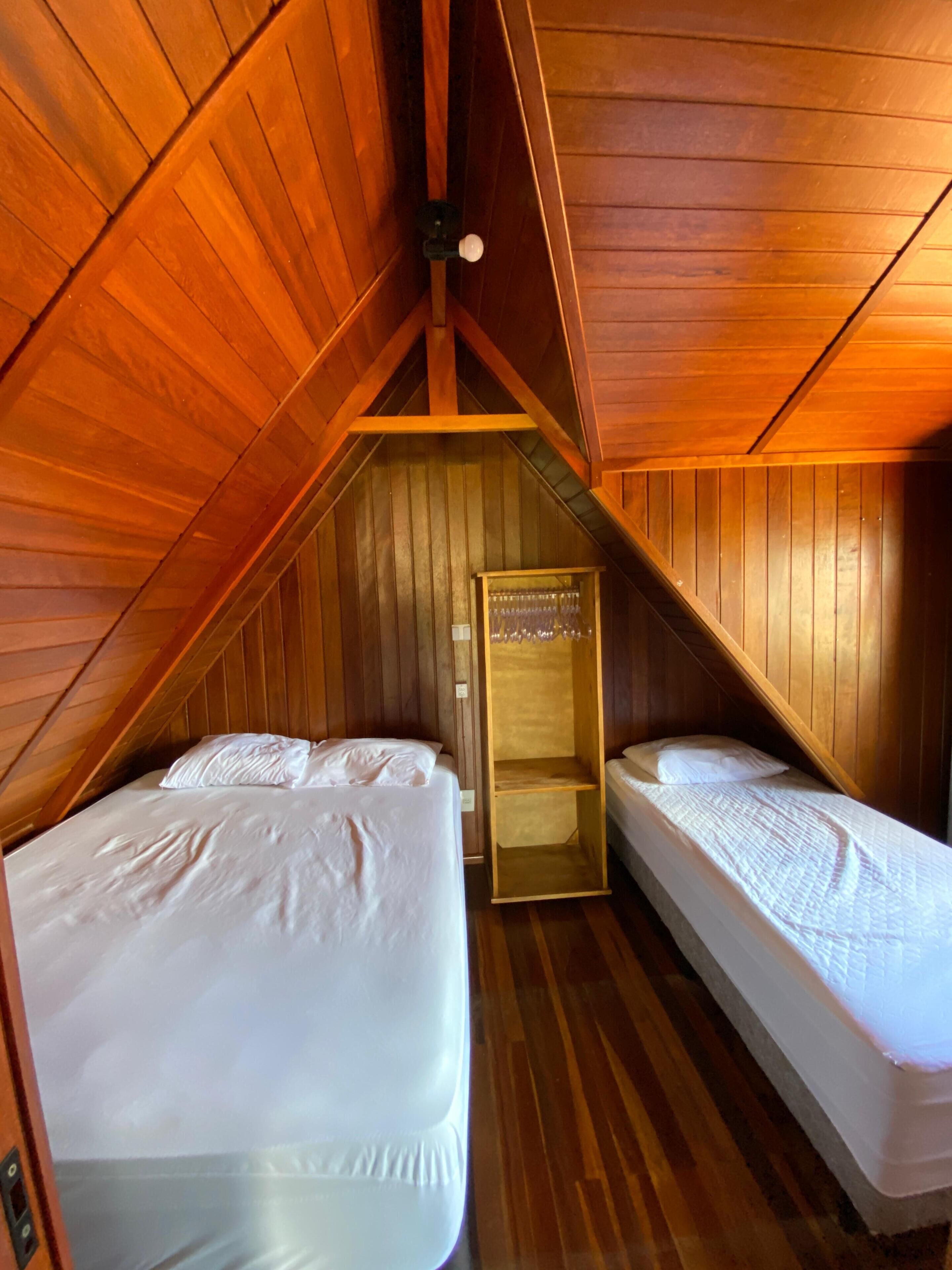 A small, wooden-paneled room with two beds, a wooden wardrobe, and a slanted ceiling.