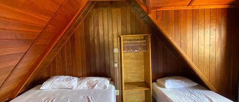 A small, wooden-paneled room with two beds, a wooden wardrobe, and a slanted ceiling.