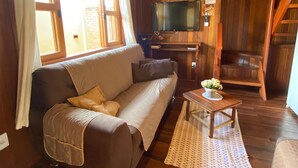A wooden interior with a sofa, a television, and a small table with flowers. - Cozy chalet in Brotas, SP - Rustic area + Air conditioning (Santa Cecilia II)