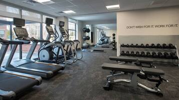 A gym with treadmills, elliptical machines, a bench press, and a wall with motivational text.