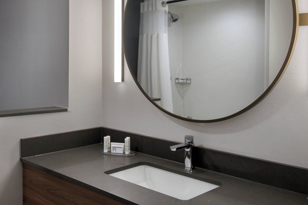 A modern bathroom with a large mirror, a white sink, and a shower area.