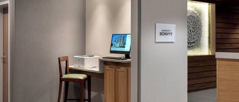 A modern hotel room with a desk, a computer, and a chair. There is a sign indicating the hotel name.
