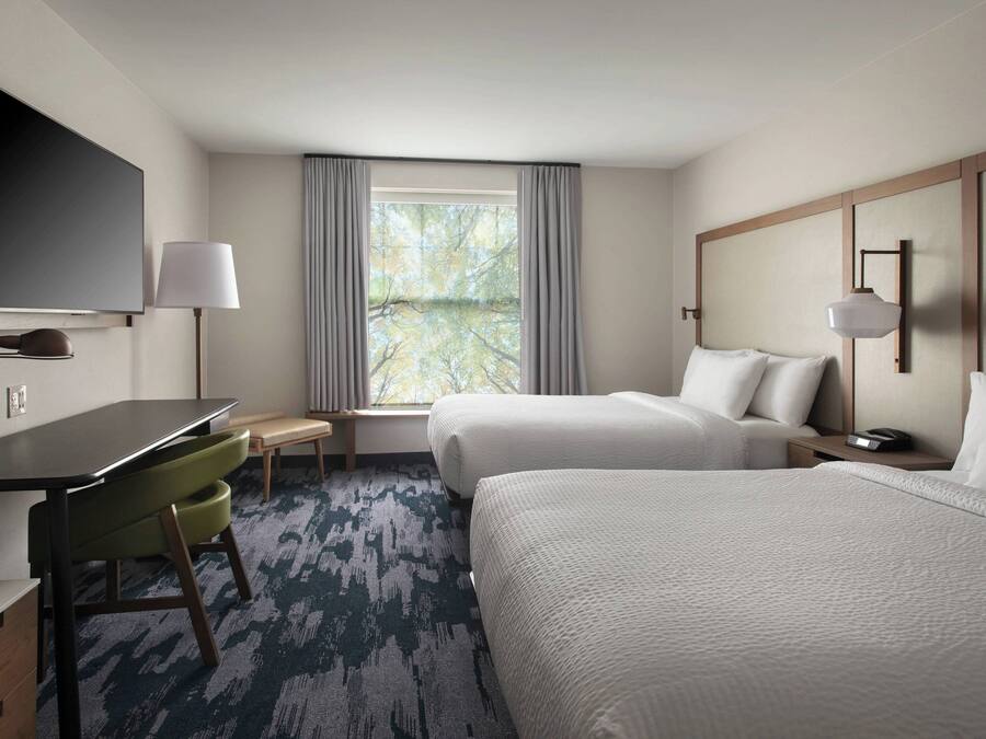 A hotel room with a bed, a desk, a chair, a TV, and a window with curtains.