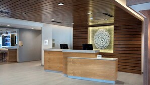 A reception area with a wooden reception desk, a bar area in the background, and a decorative wall piece. - Fairfield Inn & Suites by Marriott Williamstown (Williamstown)