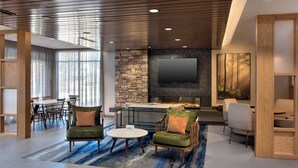 A modern living room with a fireplace, comfortable seating, a flat-screen TV, and a stone accent wall. - Fairfield Inn & Suites by Marriott Williamstown (Williamstown)
