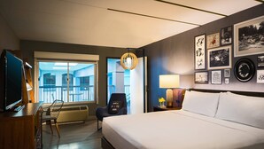 Une chambre d’hôtel comprenant un lit, un bureau avec une télévision, une chaise, un balcon avec vue et des œuvres d’art aux murs.