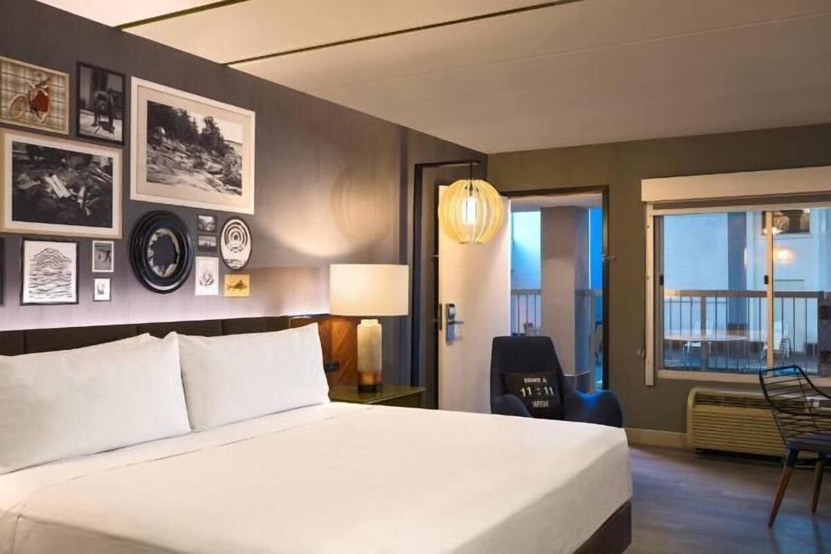 A hotel room with a large bed, a desk, a chair, a lamp, and a window with a view.