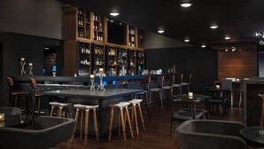 Una zona de bar con una barra de madera oscura, varios taburetes y una estantería repleta de licores.