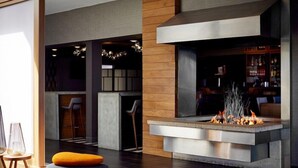 Un área de descanso moderna con una chimenea central, asientos y un bar al fondo.