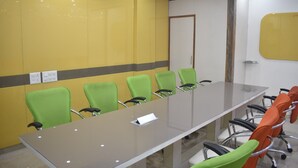 A conference room with a long table, green and orange chairs, a whiteboard, and an air conditioning unit on the wall. - S.R Residency (Dera Bassi)