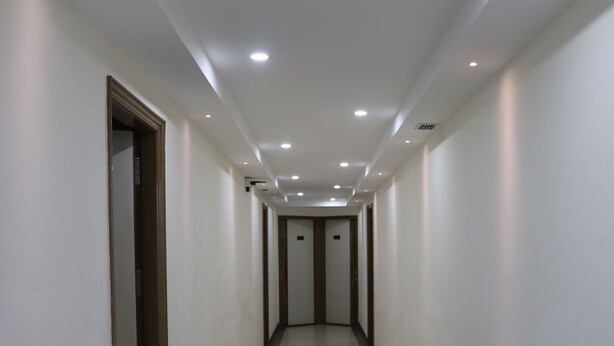 A long, narrow hallway with white walls and a tiled floor, leading to a door at the end. - S.R Residency (Dera Bassi)