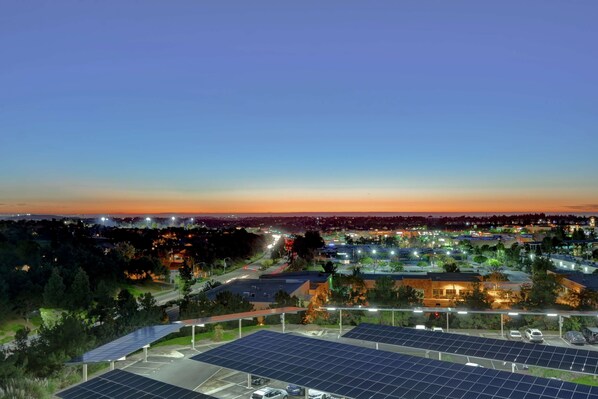 A solar panel installation at a parking lot with a view of a cityscape at dusk.