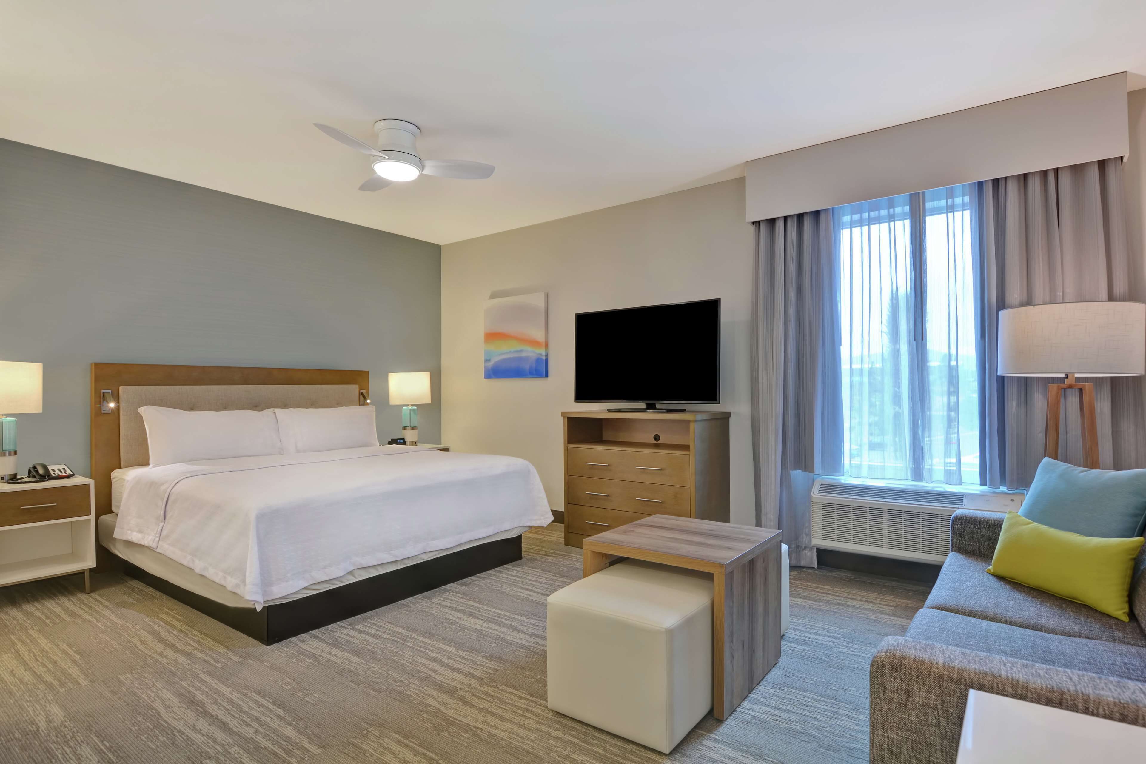 Una habitación de hotel con cama, televisión, escritorio, sofá y ventana con cortinas.