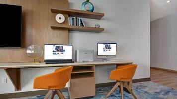 A modern workspace with a flat-screen TV, two laptops, a printer, and two orange chairs.