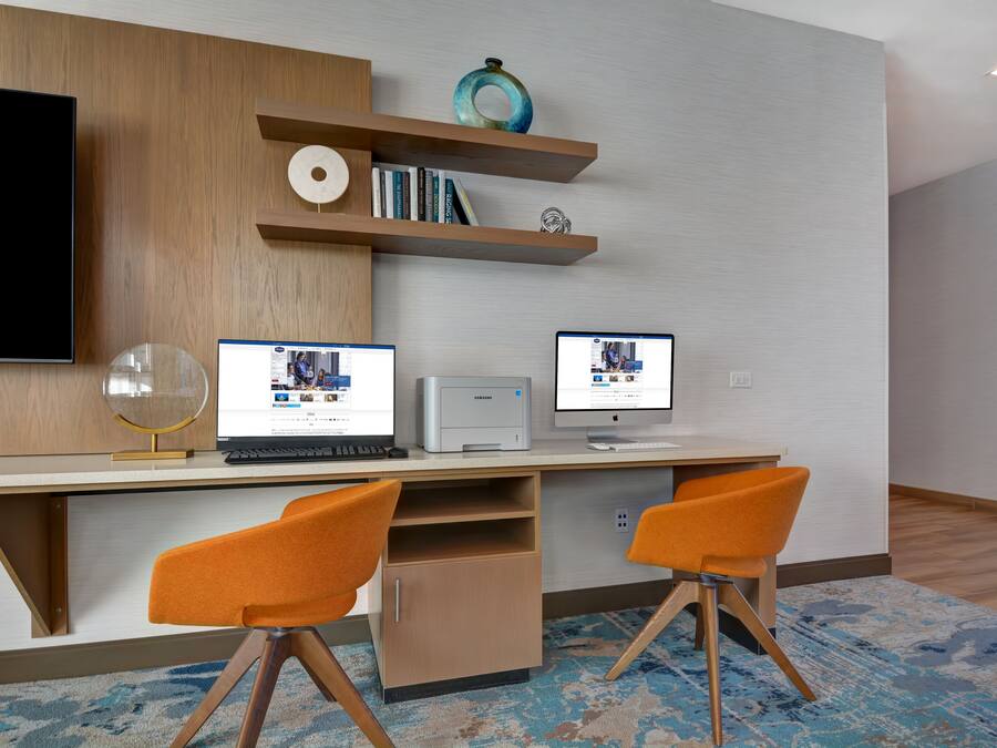 A modern workspace with a flat-screen TV, two laptops, a printer, and two orange chairs.