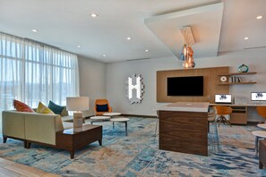 A modern hotel lobby with a sofa, chairs, a coffee table, a TV, and a desk with computers. - Homewood Suites by Hilton Chula Vista-Eastlake (Chula Vista)