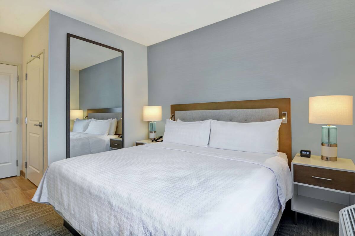 Une chambre d’hôtel avec un grand lit, une table de chevet avec une lampe, un miroir et une porte.