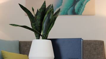 Una planta en maceta sobre una mesa con un libro titulado “Homewood Suites by Hilton” junto a un sofá con un cojín amarillo.