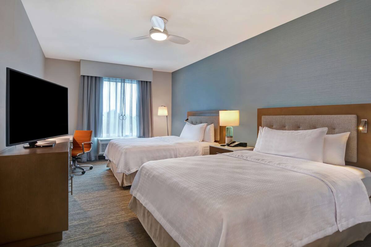 Une chambre d’hôtel avec deux lits, une télévision, un bureau et un ventilateur de plafond.