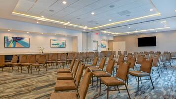 A conference room with rows of chairs, a carpeted floor, a flat-screen TV, and artwork on the walls.